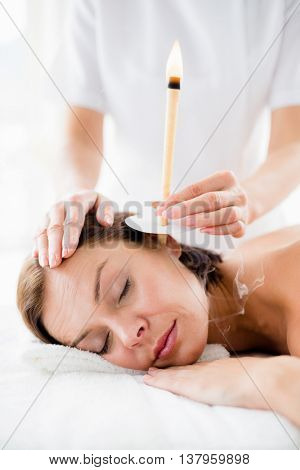 Masseur giving ear candle treament to young woman at spa