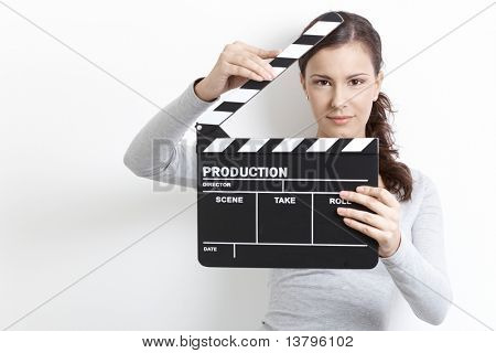 Attractive young girl holding clapper board front of her face.