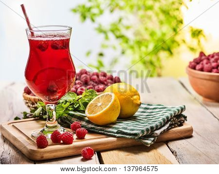 On wooden boards is ice cold beverage glass with red berries lemon cocktail . Alcohol country cocktail beverage number ninety five with raspberry clay bowl. Outdoor cocktail .
