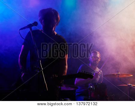 Silhouette of guitar player on stage. Dark background, smoke, spotlights