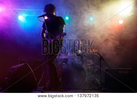 Silhouette of guitar player on stage. Dark background, smoke, spotlights
