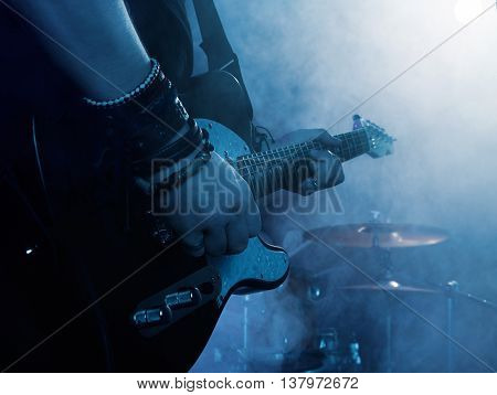 Silhouette of guitar player on stage. Dark background, smoke, spotlights