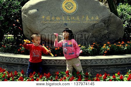 Jie Zi Ancient Town China - October 1 2010: Two small children blowing bubbles in front of a boulder with gilded letters proclaiming Jiezi to be a China Intangible Cultural Heritage Exhibition Area