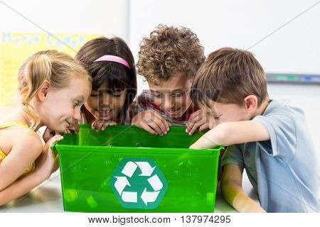 Cute children looking at plastic bottles in recycling box in classroom