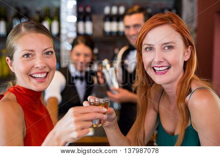 Portrait of happy friends holding a tequila shot in front of bar counter in bar