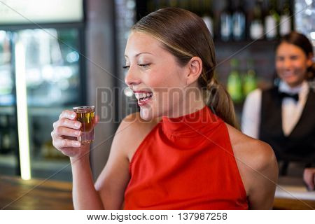 Happy woman holding a tequila shot in front of bar counter in bar