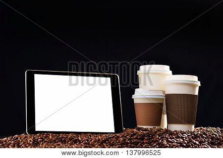 Tablet computer with blank white screen and paper cups of coffee on pile of coffee beans