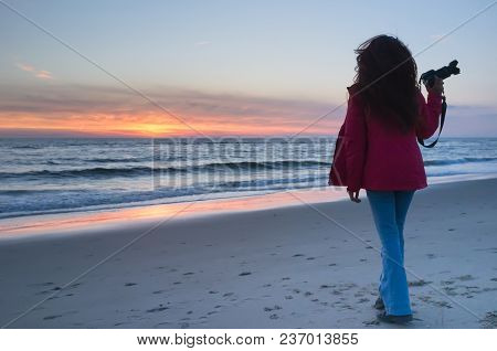Beautiful Young Girl Holding A Camera And Watching The Sunset On The Shore, Petten, Holland