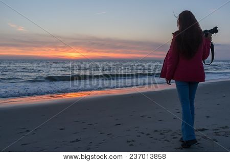 Beautiful Young Girl Holding A Camera And Watching The Sunset On The Shore, Petten, Holland
