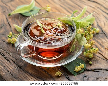 Cup of linden tea and lime flowers on the wooden table.