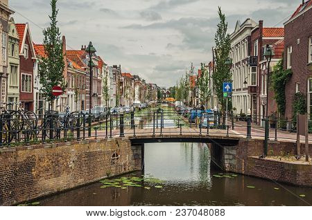 Gouda, Southern Netherlands - June 29, 2017. Long Canal With Small Bridge, Brick Houses And Cloudy D