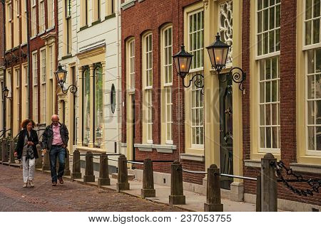 Delft, Western Netherlands - June 29, 2017. Couple Walking On Street With Elegant Semidetached Brick