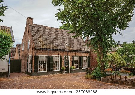 Charming And Quiet Street With Brick Rustic Houses And Greenery In Cloudy Day At Drimmelen. A Lovely