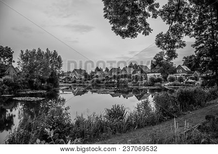 Charming Canal Next To Rustic Houses With Bushes, Lawn And Trees In Cloudy Day At Drimmelen. A Lovel