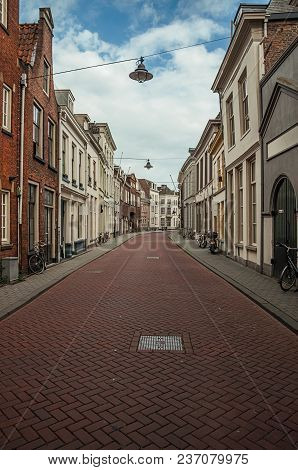Empty Street With Semidetached Brick Houses And Bicycles In Front Of Doors At Sunset And Blue Cloudy
