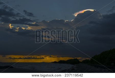 Cloud iridescence, rainbow irisation over golden sea coast line.