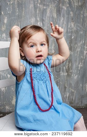 Little Girl Sitting On Chair Is Pointing On Grey Studio Background