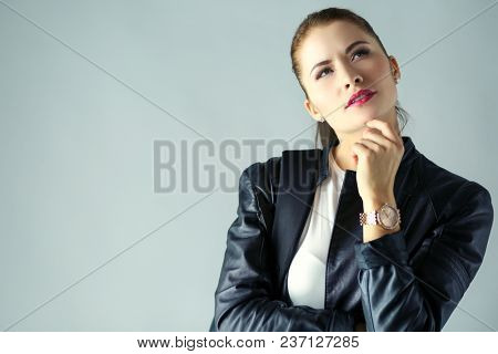 portrait of beautiful young brunette woman in stylish black jacket on gray.
