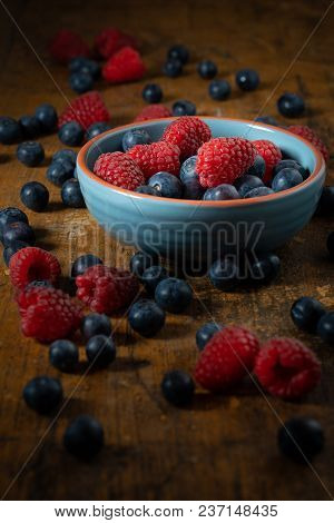 Raspberries And Blueberries In A Blue Bowl On A Rustique Table