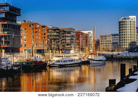 The Springtime In Hafencity Hamburg.the Ice On The Canal Reflects Ships And Buildings.