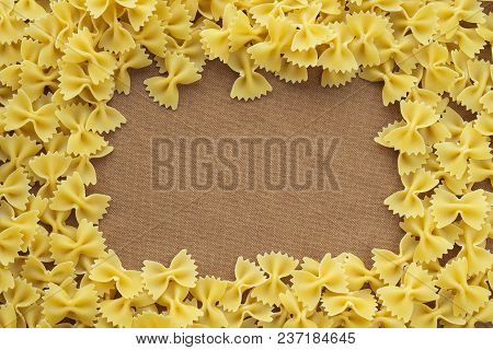 Farfalle Raw Farfallini Background Of Pasta. A Textured Wooden Cutting Board. Close-up View From The