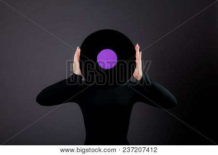 The Girl In Biack Holds A Vinyl Disk In Her Hands, Closes Her Face. Studio Photography On A Gray Bac