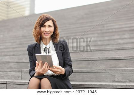 Female Caucasian Administrator Sitting On Stairs With Tablet. Concept Of Working In Open Ait And Mod