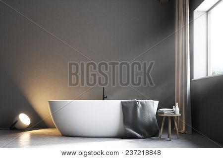 Gray Bathroom Interior With A Concrete Floor, A Large Window With Gray Curtains, And A White Bathtub