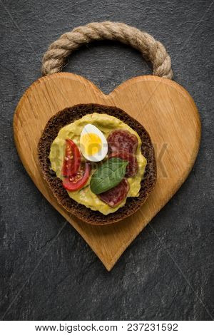 Open faced sausage sandwich canape or crostini on a wooden serving board  on dark stone background closeup. Top view.