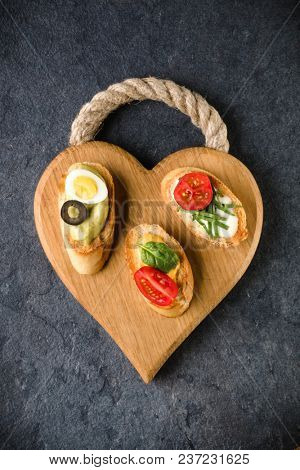 Open faced sandwich canape or crostini on a wooden serving board on dark stone background closeup. Top view. Vegetarian tartarine.