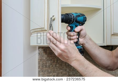 Installation Of Kitchen Furniture. A Man Is Fixing The Handles To The Curved Door Cabinets.
