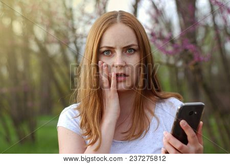 Young Women Girl Get Bad News On Smartphone Cell Phone. Womne Hold Mobile Phone. Blured Green Garden
