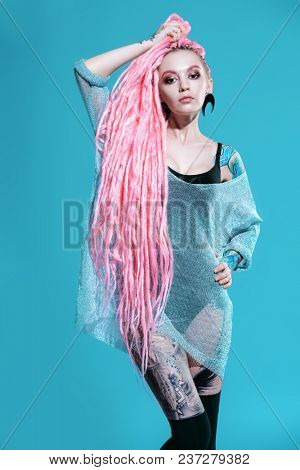 Sexy girl with pink dreadlocks posing in kombidress on a gray background. Beauty, fashion.