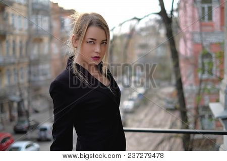 Portrait Of A Young Woman In A Black Suit Close-up Against A Background Of A Blurry City In The Rays