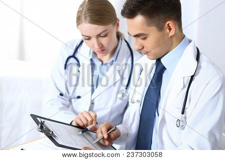 Doctors Writing Papers Using Clipboard. Physicians Discussing Medication Program Or Studying At Medi