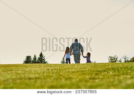Soldier With Two Little Girls Walking Forward, Back View. Father And Daughters Are Going Beyond The 
