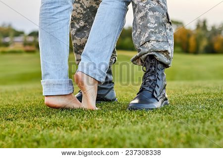 Close Up Soldier Boots And Girlfriend With Naked Feet. Standing On The Grass.