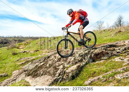 Cyclist in Red Jacket Riding the Mountain Bike Down Rocky Hill. Extreme Sport and Adventure Concept.