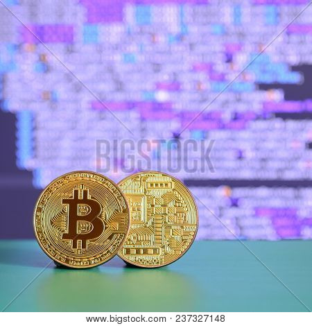 Two Gold Bitcoins Lie On The Green Surface On The Background Of The Display, Which Shows The Process