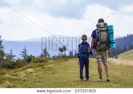Father And Son With Backpacks Hiking Together In Scenic Summer Green Mountains. Dad And Child Standi