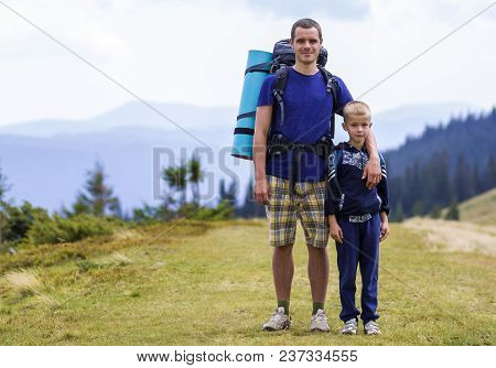 Father And Son With Backpacks Hiking Together In Scenic Summer Green Mountains. Dad And Child Standi