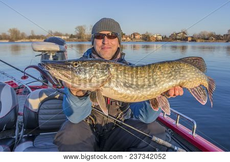 Happy Fisherman With Big Pike Fish Trophy At The Boat With Fishing Tackles