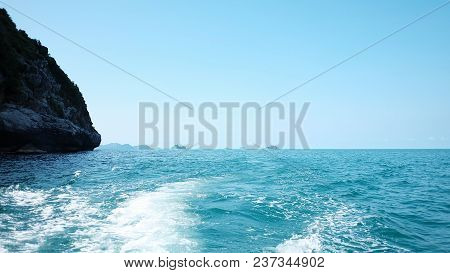 White bubles of a water waves in the deep blue sea at the south of Thailand with small island along the horizontal line and blue sky white fluffy clouds