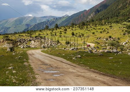 Colorful View Of Green And Snowy Mountains With Elbrus Summit Under Fluffy White Clouds.