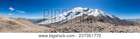 Colorful View Of Green And Snowy Mountains With Elbrus Summit Under Fluffy White Clouds.