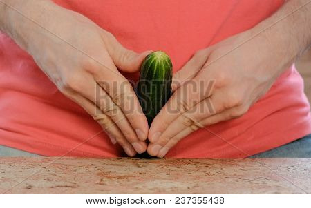 Man Plays With A Cucumber Between His Legs Standing Near The Table. Cucumber Closeup