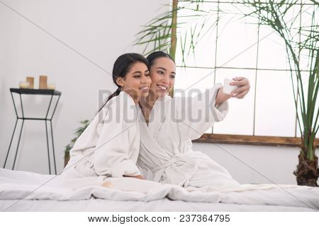 Our Photo. Positive Young Woman Holding Her Smartphone While Taking A Selfie With A Girlfriend