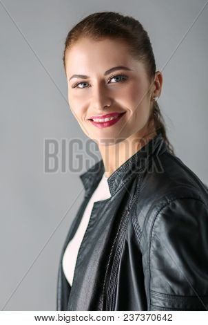 portrait of beautiful young brunette woman in stylish black jacket on gray.