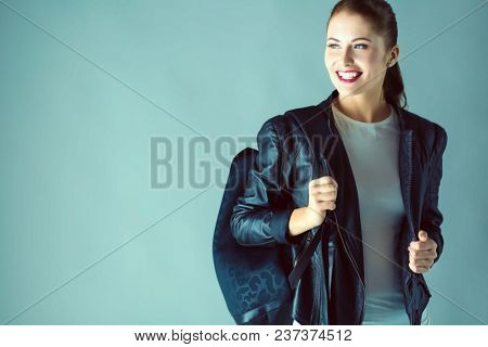 portrait of beautiful young brunette woman in stylish black jacket on gray.