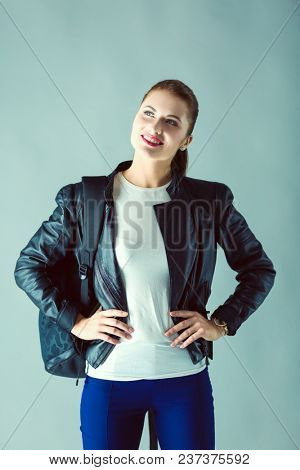 portrait of beautiful young brunette woman in stylish black jacket on gray.